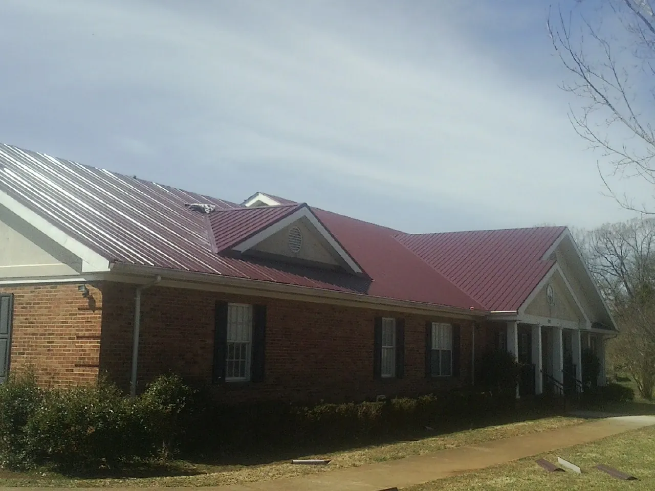 Red metal roof with gabled entries on a long brick building, from a Hail Damage Roof Repair job in Jefferson City